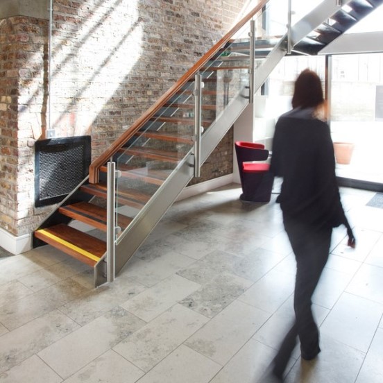 Person walking through the lobby area of the Digital Court building. There is a red chair and a staircase in the background.