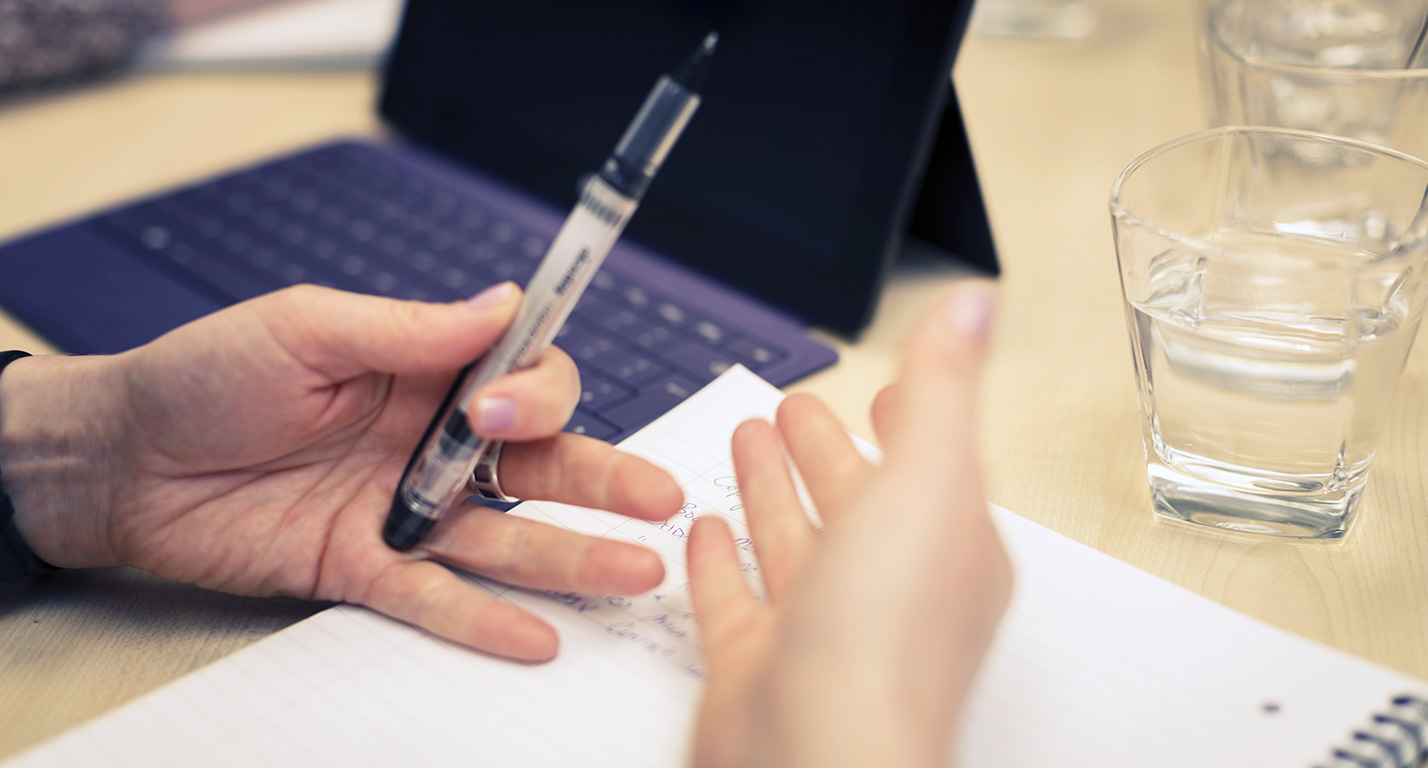 A person's hand gesture as they take notes during a meeting.