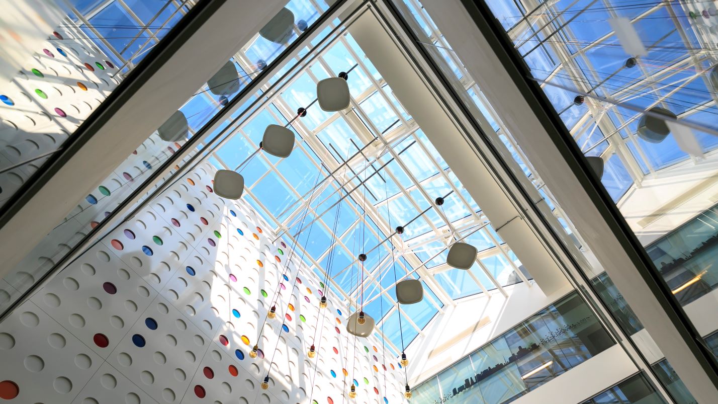 Looking up towards the window on the roof. The sky outside is blue, and looking up one also sees the colourful dots on the wall and square lampshades hanging from the ceiling.